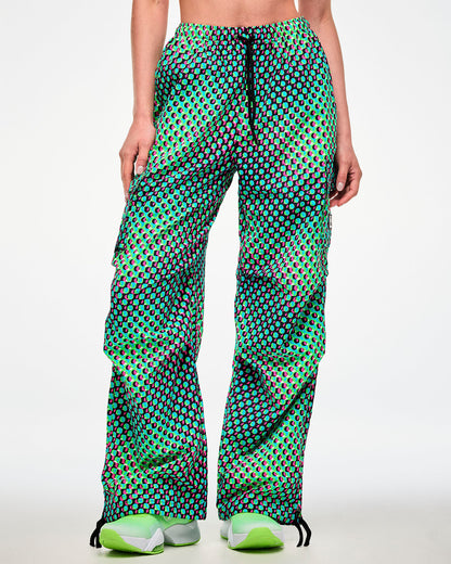 Female model wearing green cargo pants with black drawcords hanging over the aqua, black, and pink dot print, paired with green sneakers.