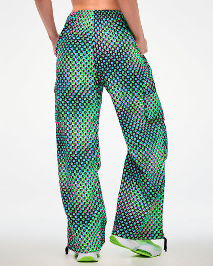 Shown from the back, female model wearing green cargo pants with an aqua, black, and pink dot print and green sneakers.