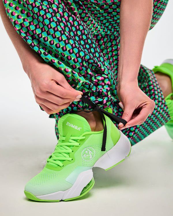 Close-up of hands cinching the drawstring ankle cuff on green cargo pants with an aqua, black, and pink dot print, paired with green sneakers.