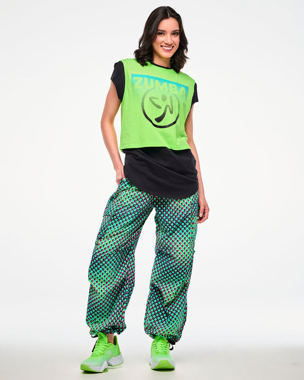 Female model wearing a neon green and black layered tee, paired with green cargo pants featuring an aqua, black, and pink dot print and green sneakers.