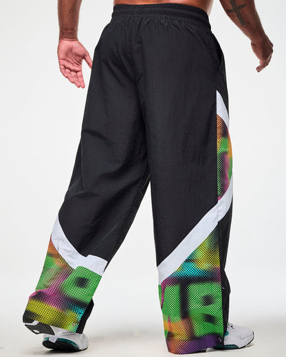 Shown from the back, male model wearing black track pants with a white and multicolor dot-print side panel and white sneakers.