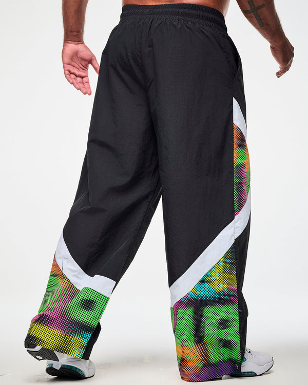 Shown from the back, male model wearing black track pants with a white and multicolor dot-print side panel and white sneakers.