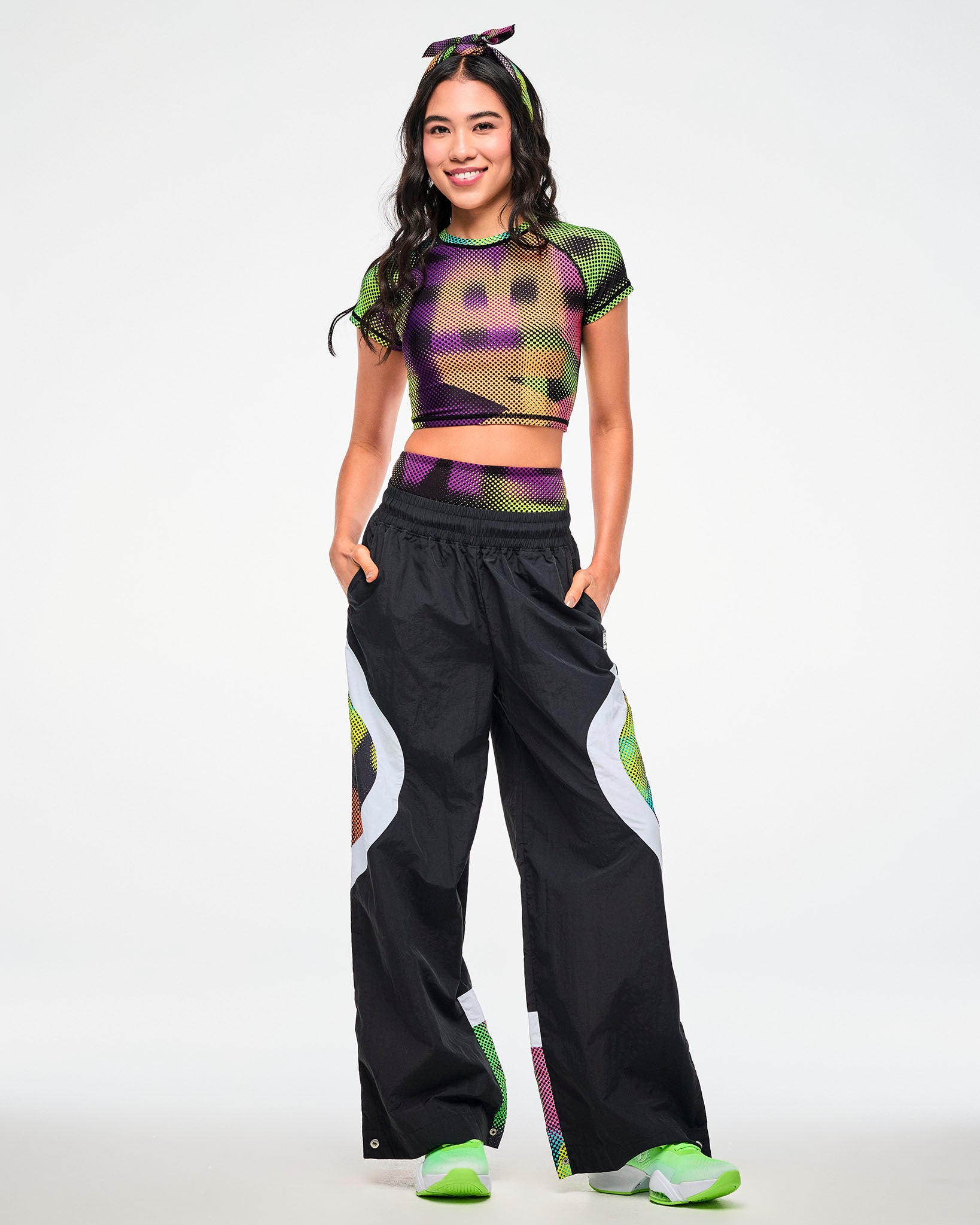 Female model wearing a dot-print crop top, paired with black track pants featuring a matching dot-print side panel and green sneakers.