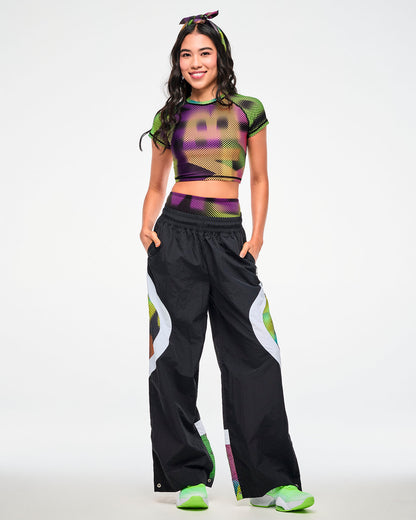 Female model wearing a dot-print crop top, paired with black track pants featuring a matching dot-print side panel and green sneakers.