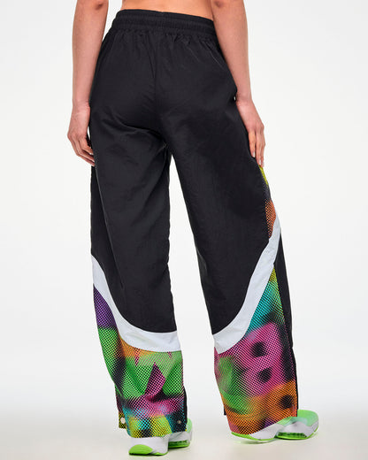 Shown from the back, female model wearing black track pants with a dot-print side panel and green and white sneakers.