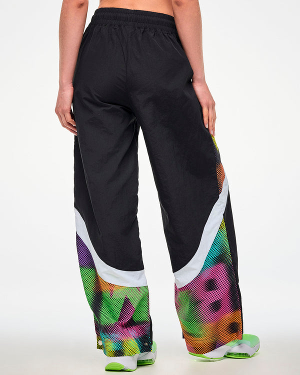 Shown from the back, female model wearing black track pants with a dot-print side panel and green and white sneakers.
