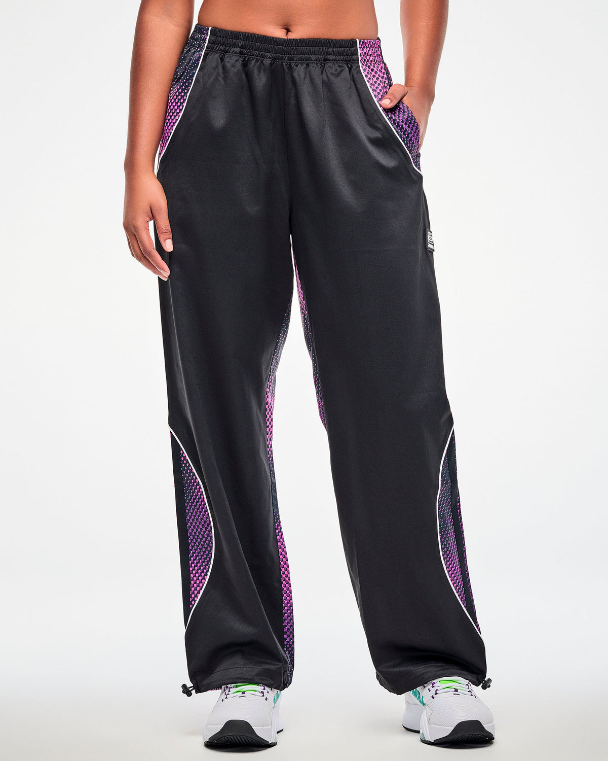 Female model wearing black track pants with a purple-to-pink dot gradient side and back panel, paired white white shoes.