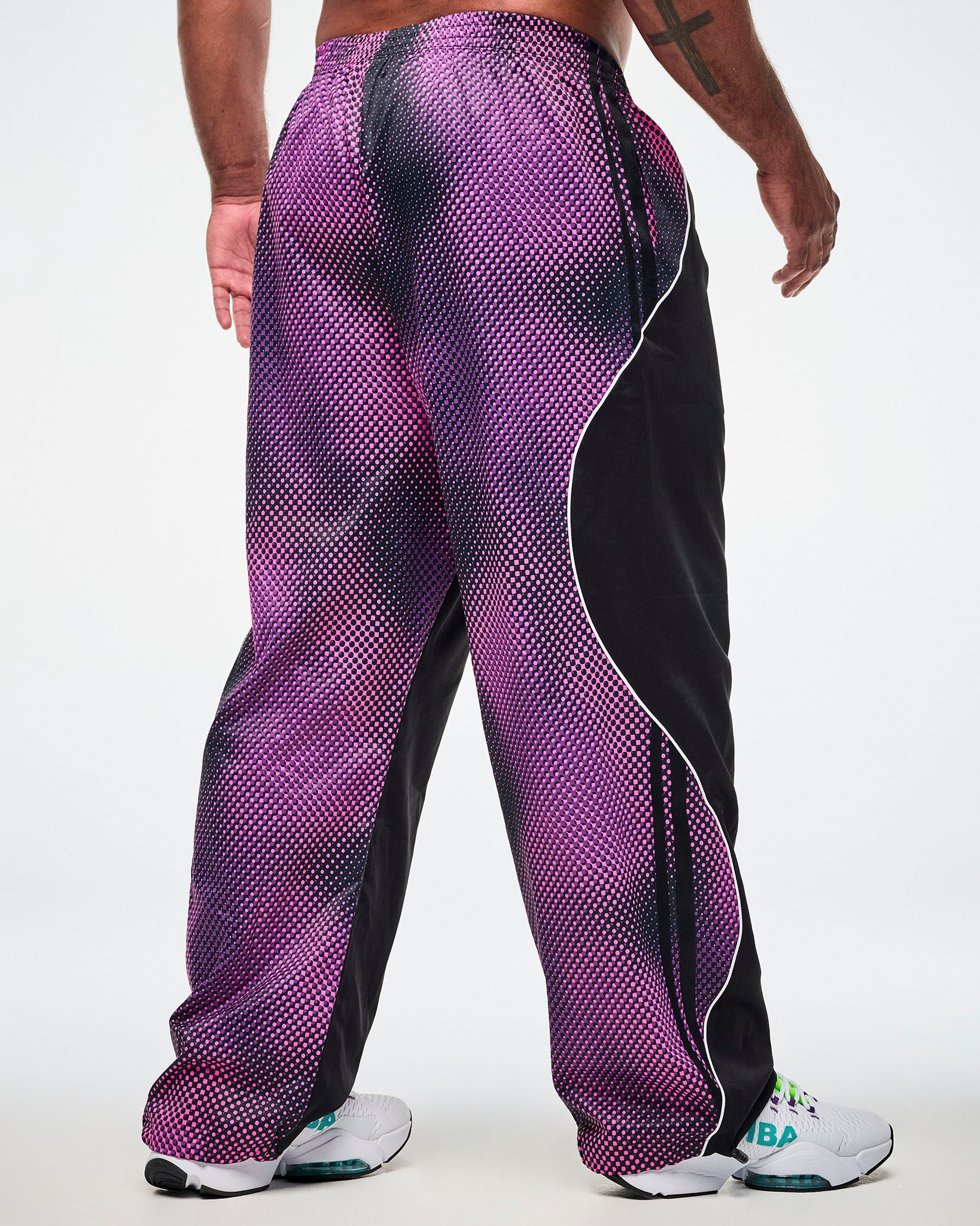 Shown from the back, male model wearing black pants with a purple-to-pink dot gradient side and back panel and white sneakers.