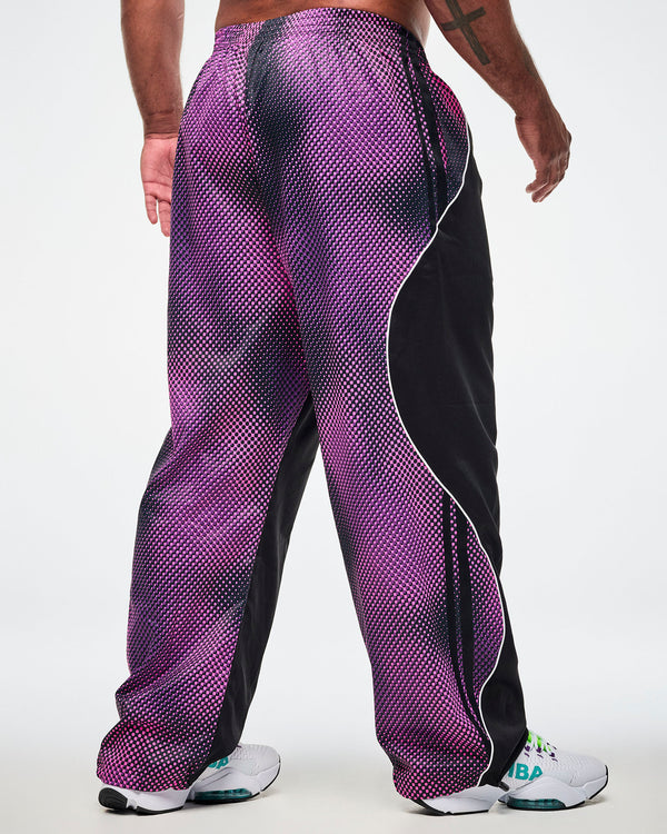 Shown from the back, male model wearing black pants with a purple-to-pink dot gradient side and back panel and white sneakers.