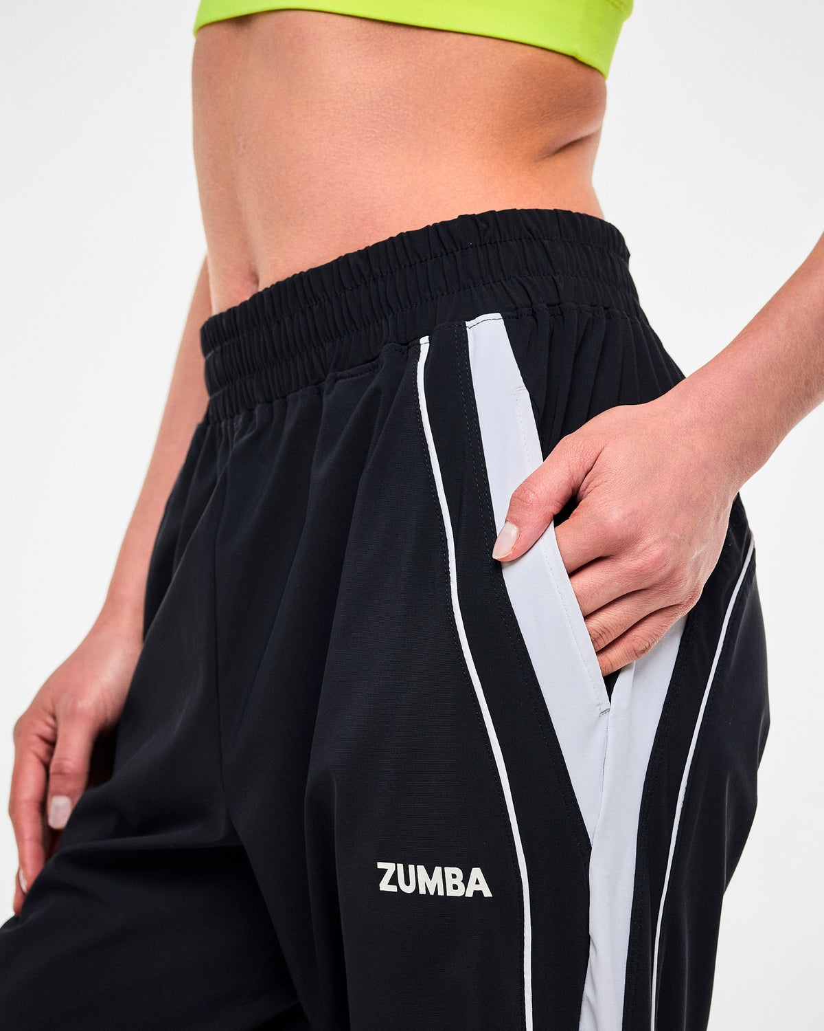 Close-up of a hand in the side pocket of black joggers with a white stripe and "ZUMBA" text in white on the left side.