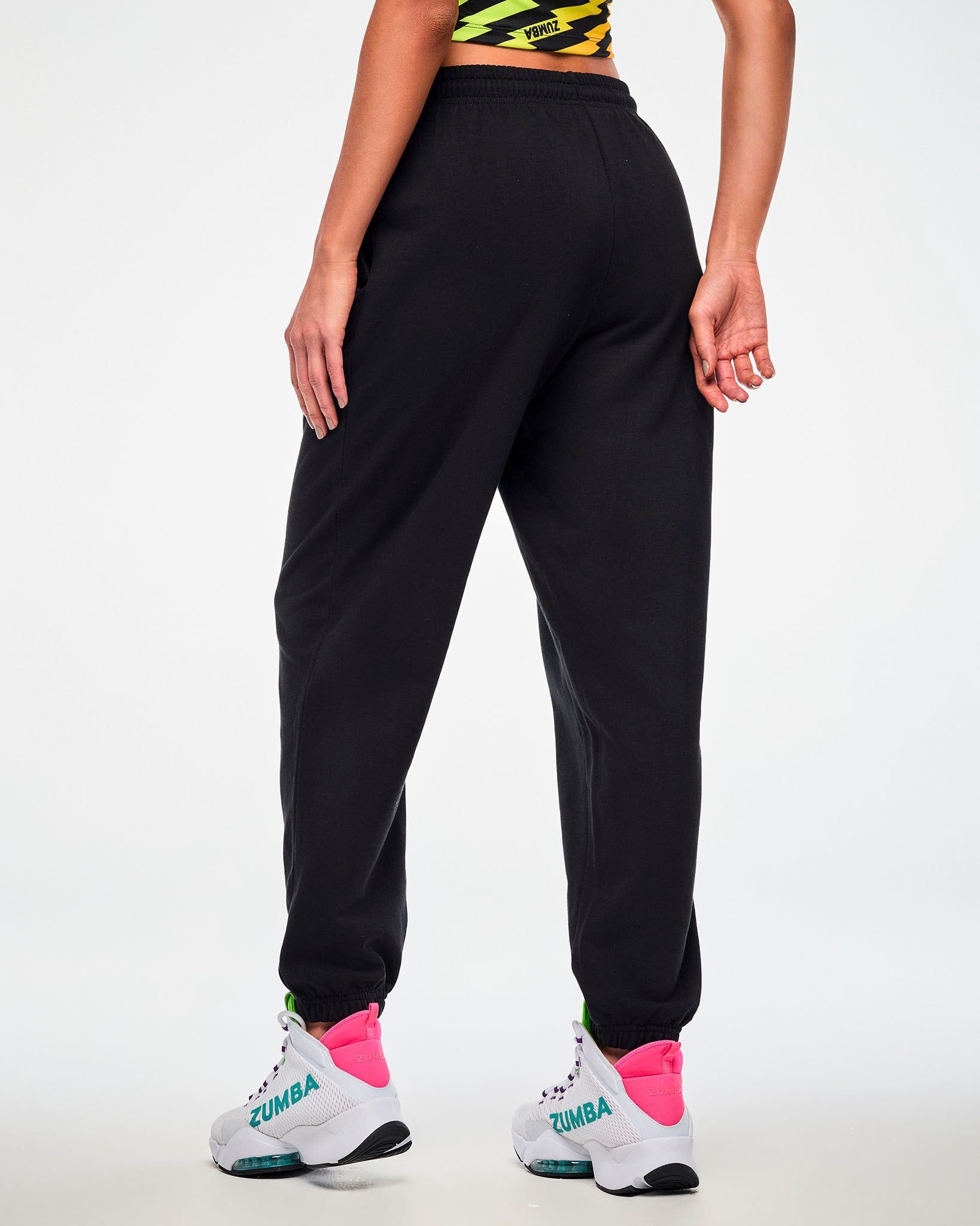 Shown from the back, female model wearing black joggers and white sneakers.