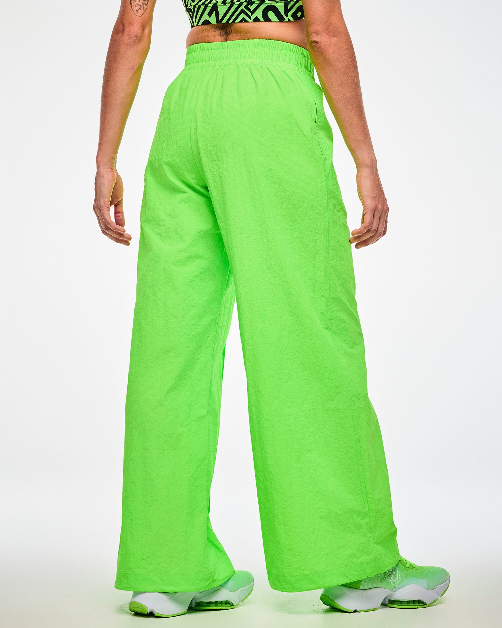 Shown from the back, female model wearing green wide-leg track pants and green shoes.