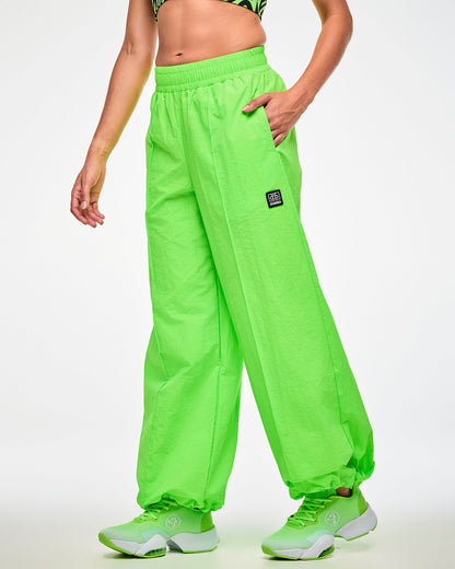 Female model wearing lime green wide-leg track pants and green shoes, cassette tag patch visible at the hip and hand in the same side pocket.
