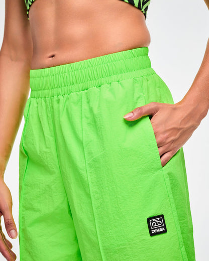 Close-up of female model hand in her pocket of the green track pants and the cassette tag patch below the pocket.