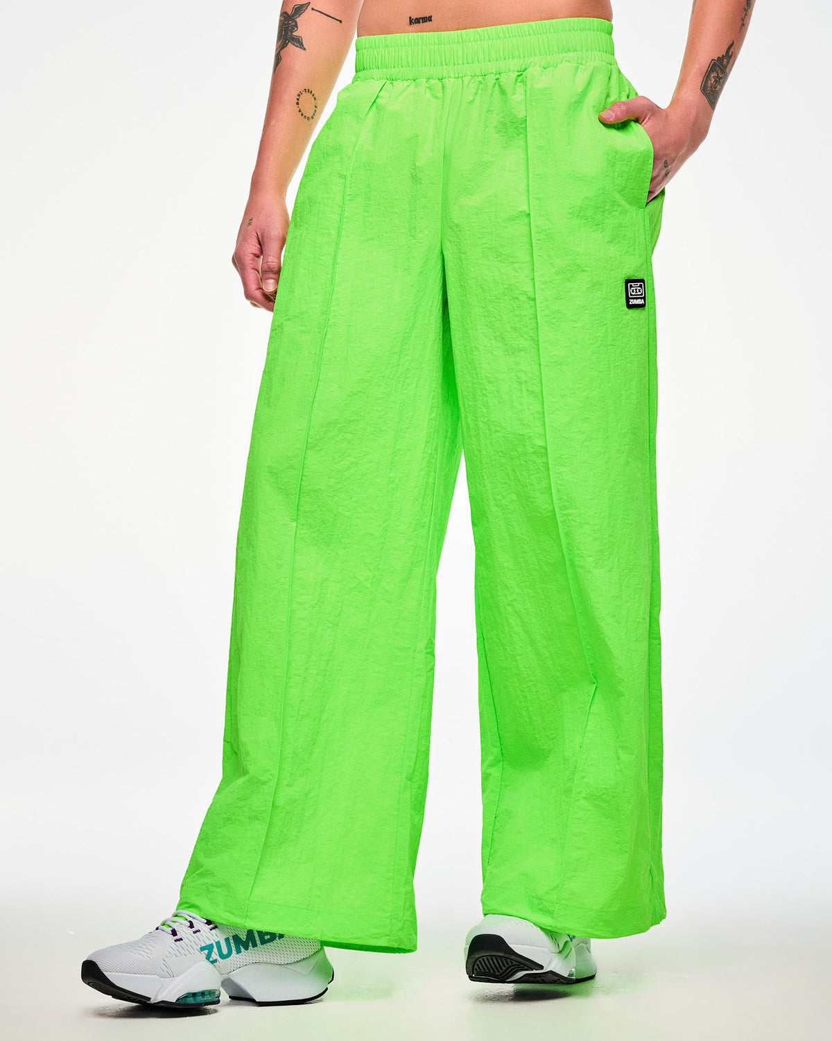 Male model wearing lime green wide-leg track pants, hand in the pocket and paired with white shoes.