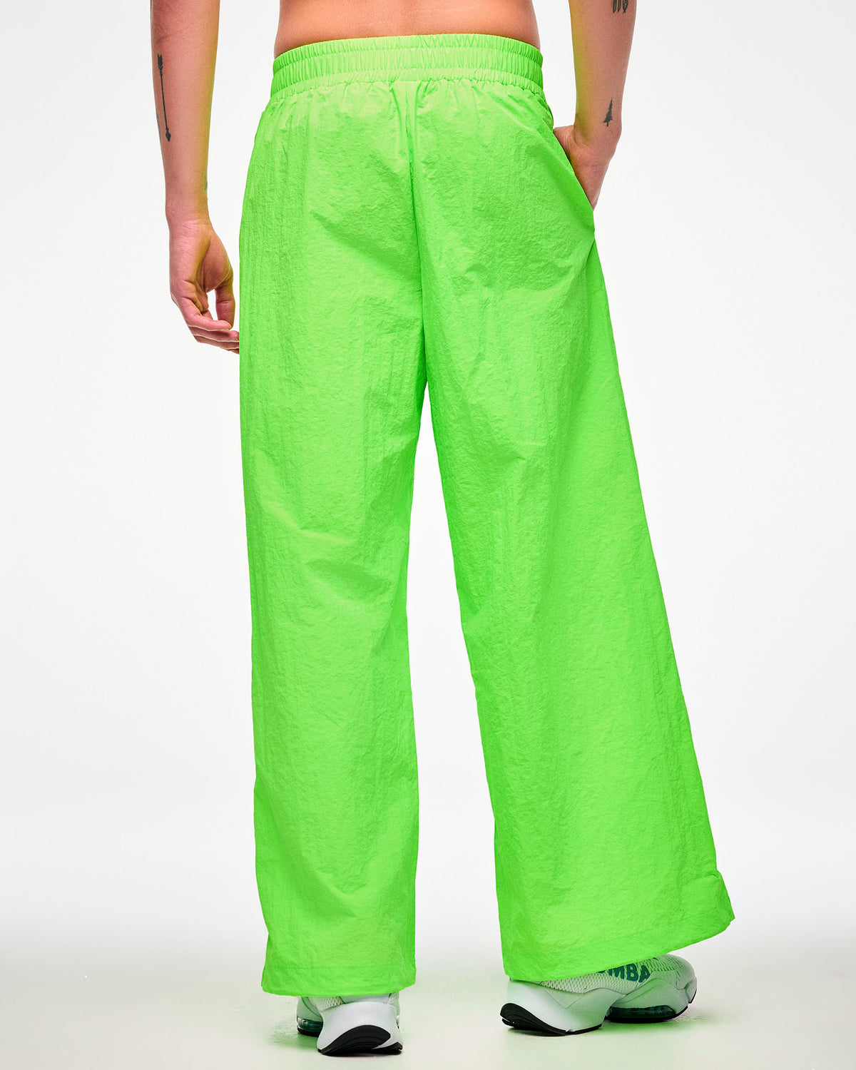 Shown from the back, male model wearing green wide-leg track pants and white shoes, hand in the side pocket.