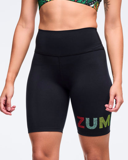Black high-waisted biker shorts with a wide waistband and multicolor “ZUM” logo on the lower leg, shown on a female model from the front against a white background.