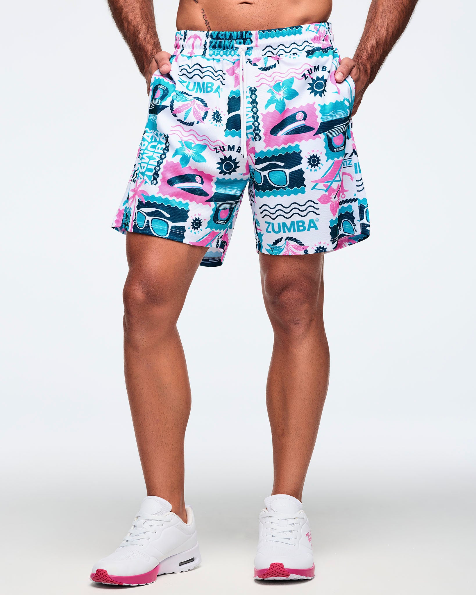 Front view of white elastic-waist drawstring shorts with a teal-and-pink Zumba graphic print and white drawcord; shown on a male model with white sneakers.