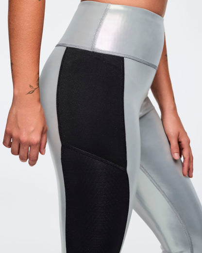 Metallic silver high-waisted leggings with black side panels and curved seam detailing. Female model wears fitted glossy full-length leggings with a wide waistband, shown in a close side view against a light gray background.