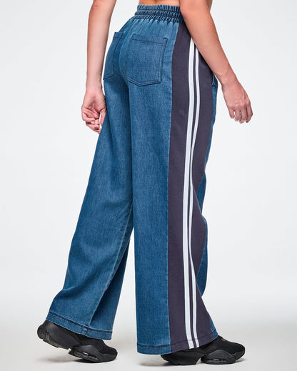 Back view of a female model wearing wide-leg pants, showing the denim back pockets and navy side panel with a double white stripe.