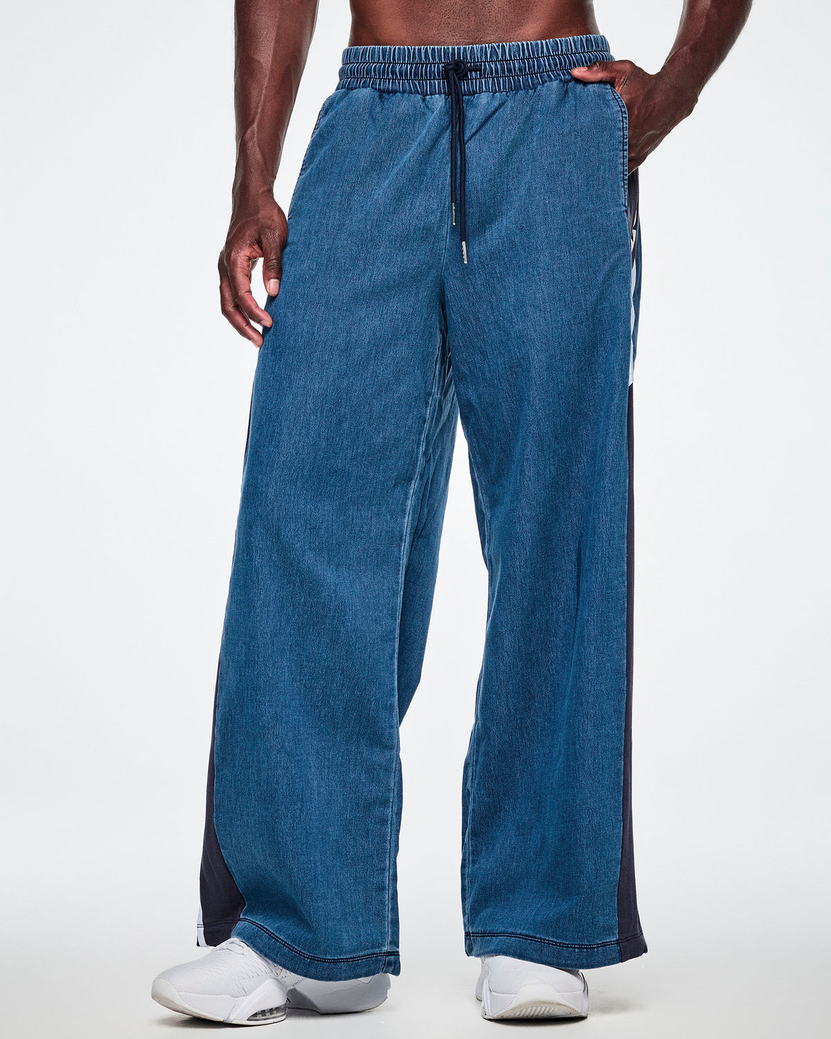 Front view of a male model with his hands in the side pockets of wide-leg combo pants, showing the denim front and paired with white shoes.