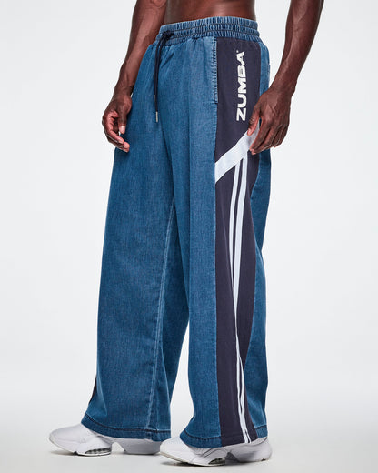 Close-up front view of a male model wearing wide-leg combo pants, showing the navy side panel with white "ZUMBA" text, a diagonal white stripe, and two vertical white stripes down the leg.