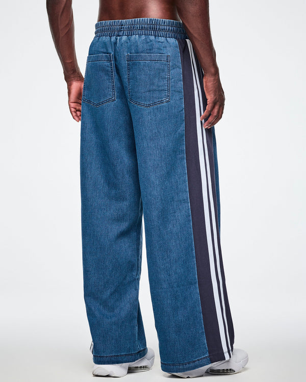 Back view of a male model wearing wide-leg combo pants, showing the denim back pockets and navy side panel with a double white stripe.