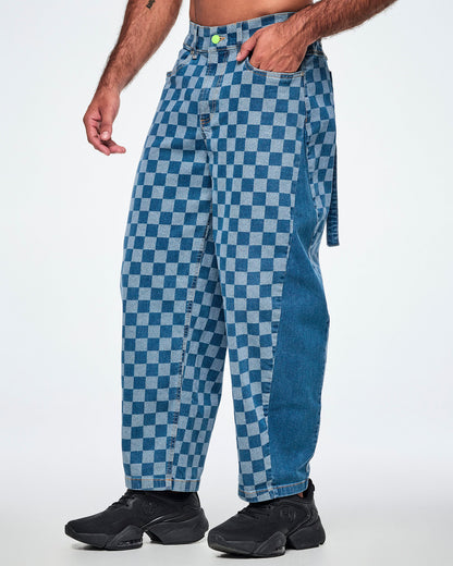 Male model in the checkerboard barrel ankle pants shown in side view, with his hand in the front pocket, a solid medium blue denim panel down the outer leg, and a denim strap hanging at the back.