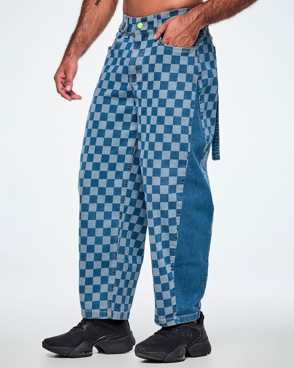 Male model in the checkerboard barrel ankle pants shown in side view, with his hand in the front pocket, a solid medium blue denim panel down the outer leg, and a denim strap hanging at the back.