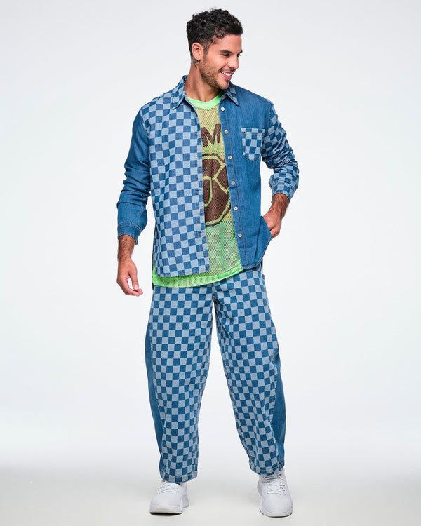 Full view of a male model in the checkerboard barrel ankle pants with a matching checkerboard and solid denim button-up worn open over a lime green mesh top, with white shoes.