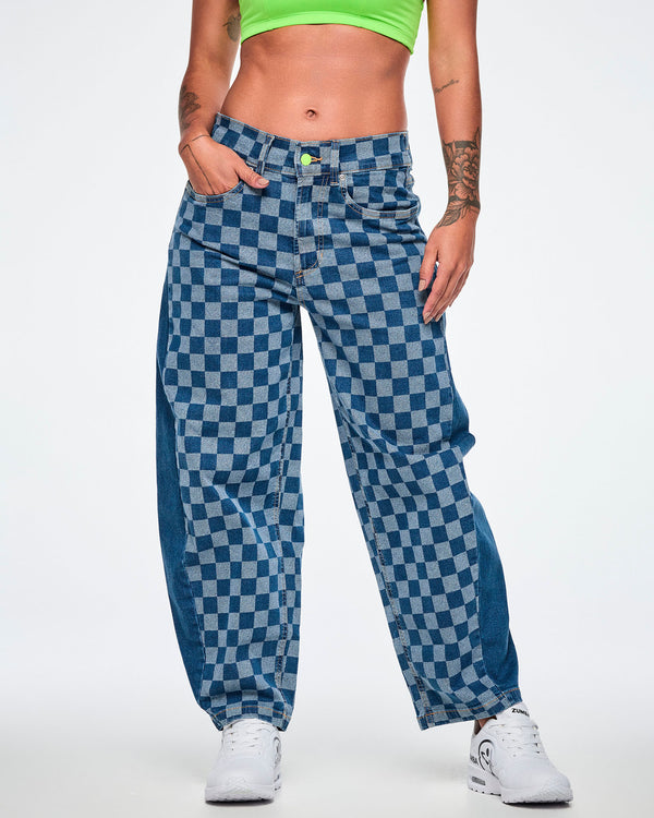 Female model with her hand in the front pocket of the barrel ankle pants in a light and medium blue checkerboard pattern, featuring a lime green button, solid denim side panels and paired with a lime green bra and white shoes.
