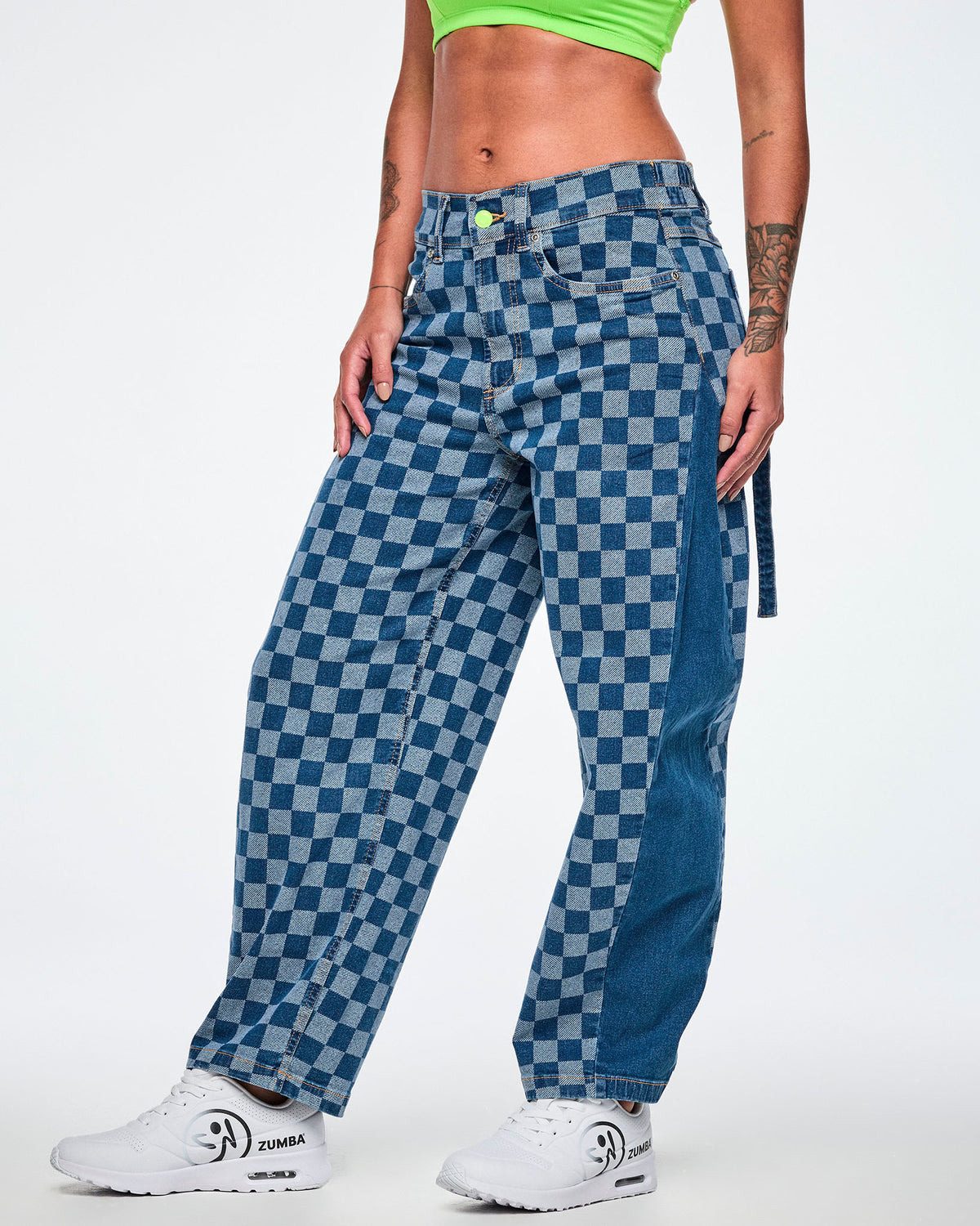Female model in the checkerboard barrel ankle pants shown in side view, highlighting the solid denim outer panel and a denim strap hanging at the back, with white shoes.