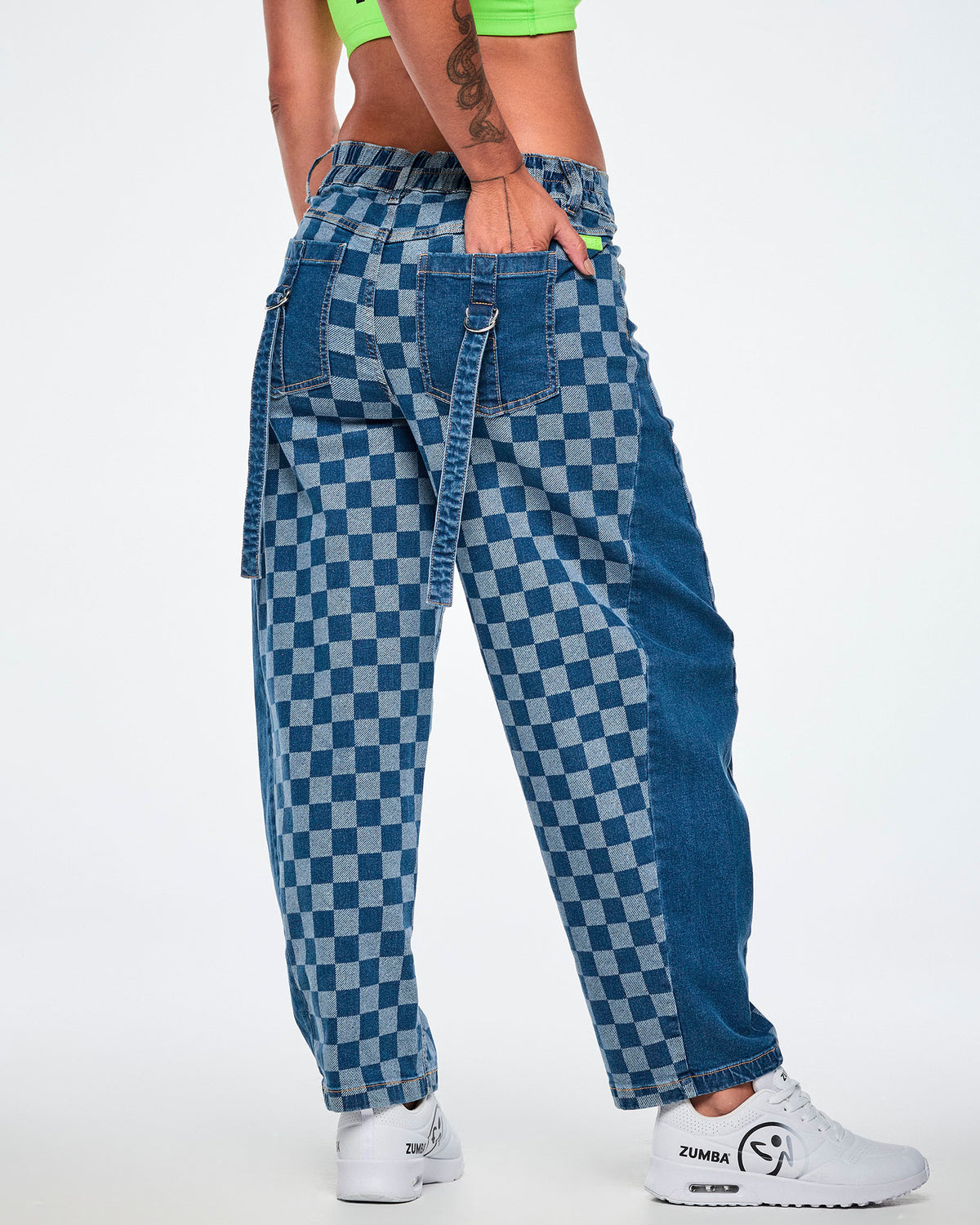 Shown from the back, a female model in the barrel ankle pants with a hand in the back pocket, showing the elastic waistband, straps with silver D-rings on the back pockets, and the rounded barrel legs, all paired with white shoes.