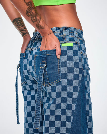 Close-up of the back of the barrel ankle pants, showing the lime green rubber 'ZUMBA' patch at the waistband and solid denim back pockets, with denim straps looped through silver D-rings.