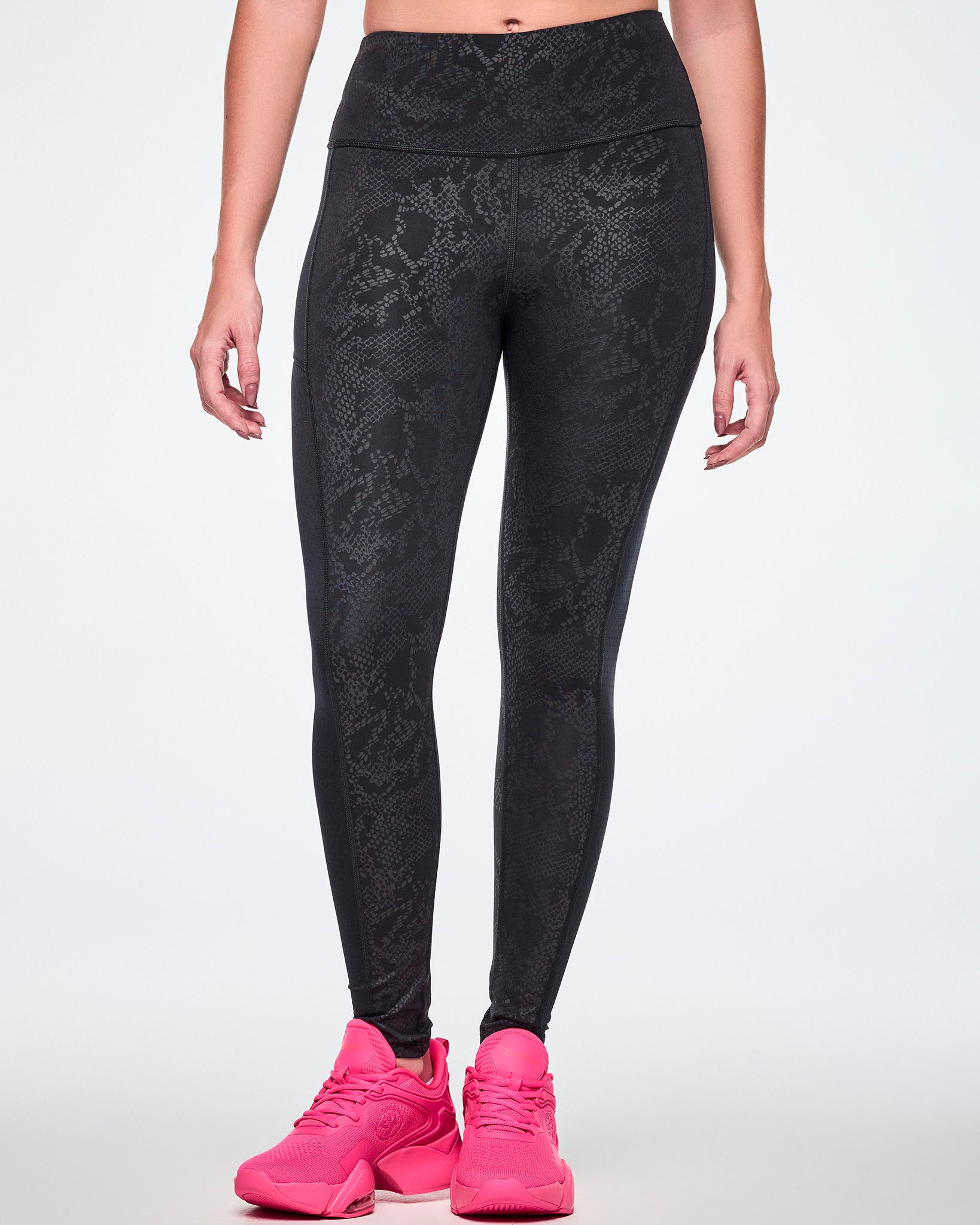 Front view of a female model wearing black high-waisted leggings with a subtle tonal snake-skin pattern and sheer mesh side panels, paired with pink shoes.