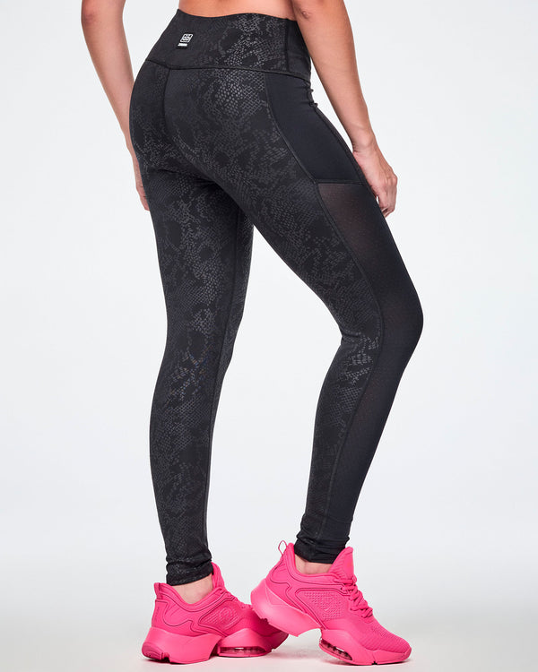 Back view of a female model wearing black high-waisted leggings with a subtle tonal snake-skin pattern and sheer mesh side panels, paired with pink shoes.