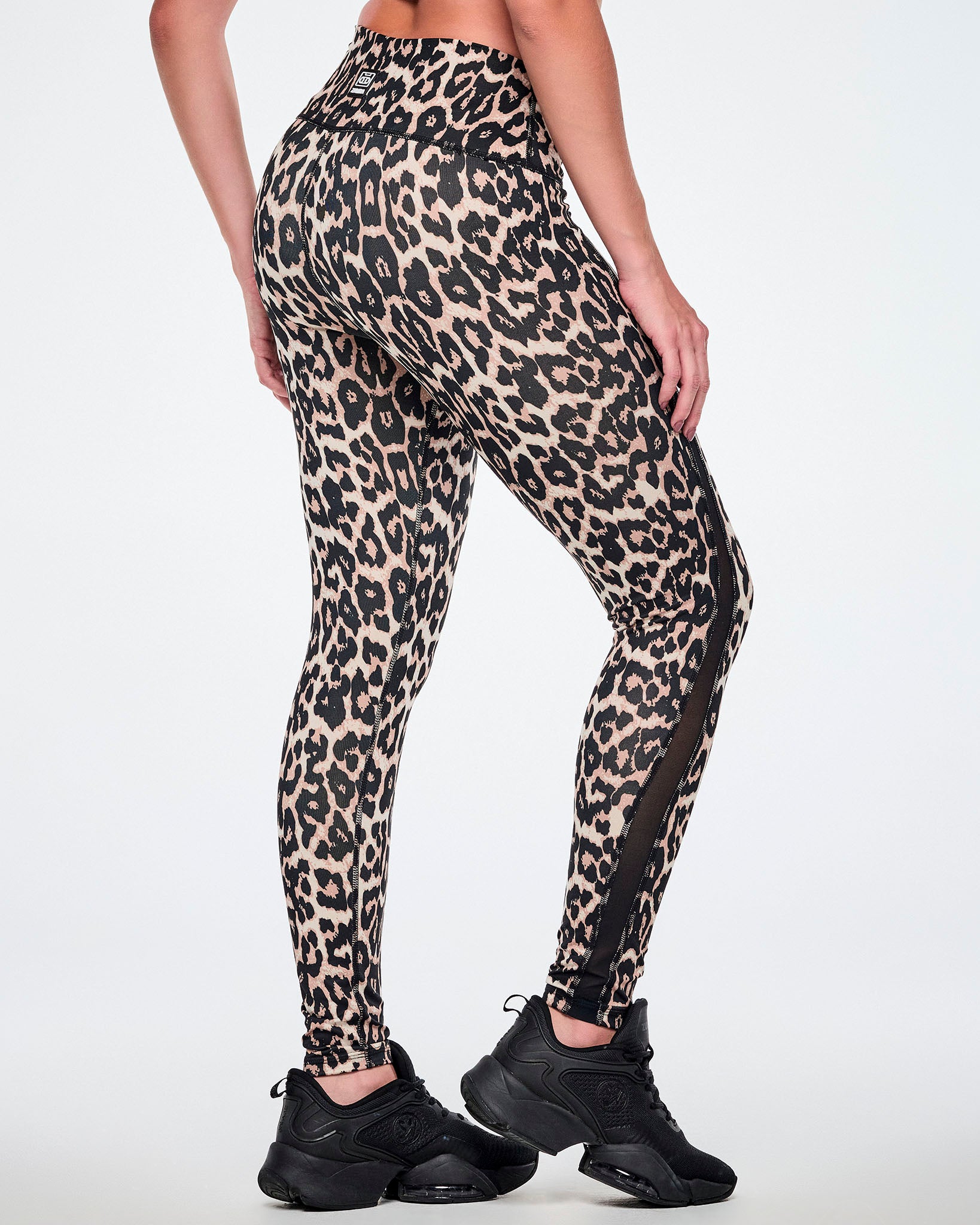 Back view of a female model wearing high-waisted leopard print leggings with sheer side panels, paired with black shoes.
