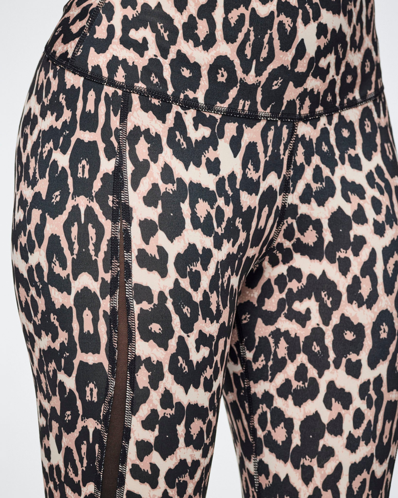 Close-up of leopard-print leggings with a black and beige pattern and side mesh panels, shown on a female model.