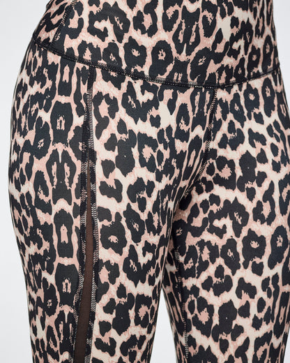 Close-up of leopard-print leggings with a black and beige pattern and side mesh panels, shown on a female model.