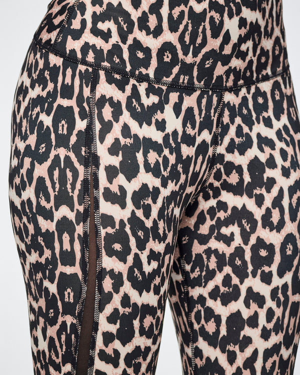 Close-up of leopard-print leggings with a black and beige pattern and side mesh panels, shown on a female model.