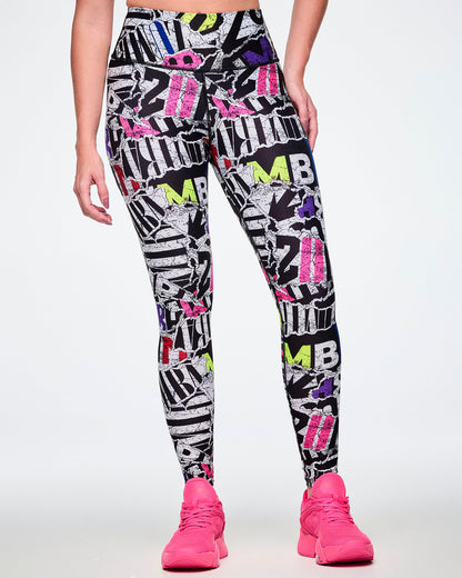 Front view of a female model wearing high-waisted leggings with a bold multicolor graffiti-style print featuring black, white, purple, blue, red, and pink lettering, paired with bright pink shoes.