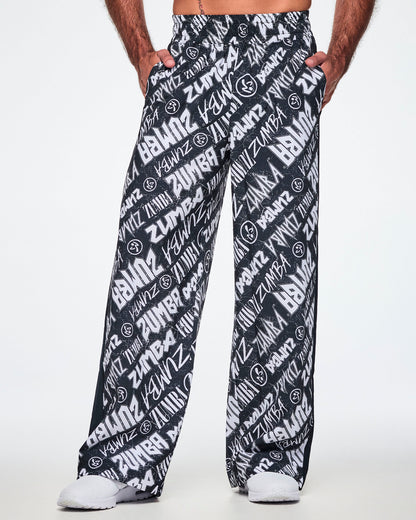 Front view of a male model wearing black and white Zumba rock branded track pants and paired with white shoes.