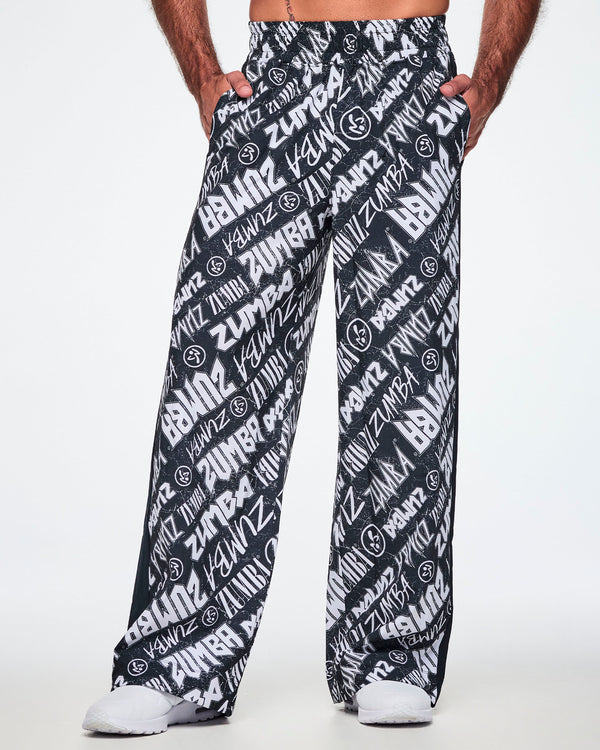 Front view of a male model wearing black and white Zumba rock branded track pants and paired with white shoes.