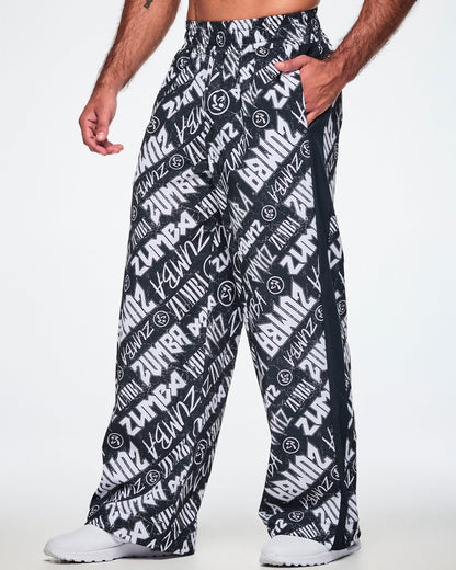 A male model wearing black and white Zumba rock branded track pants, with a black stripe down the side and paired with white shoes.