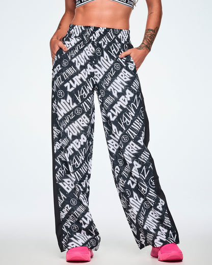 Front view of a female model wearing black and white Zumba rock branded track pants, paired with bright pink shoes.