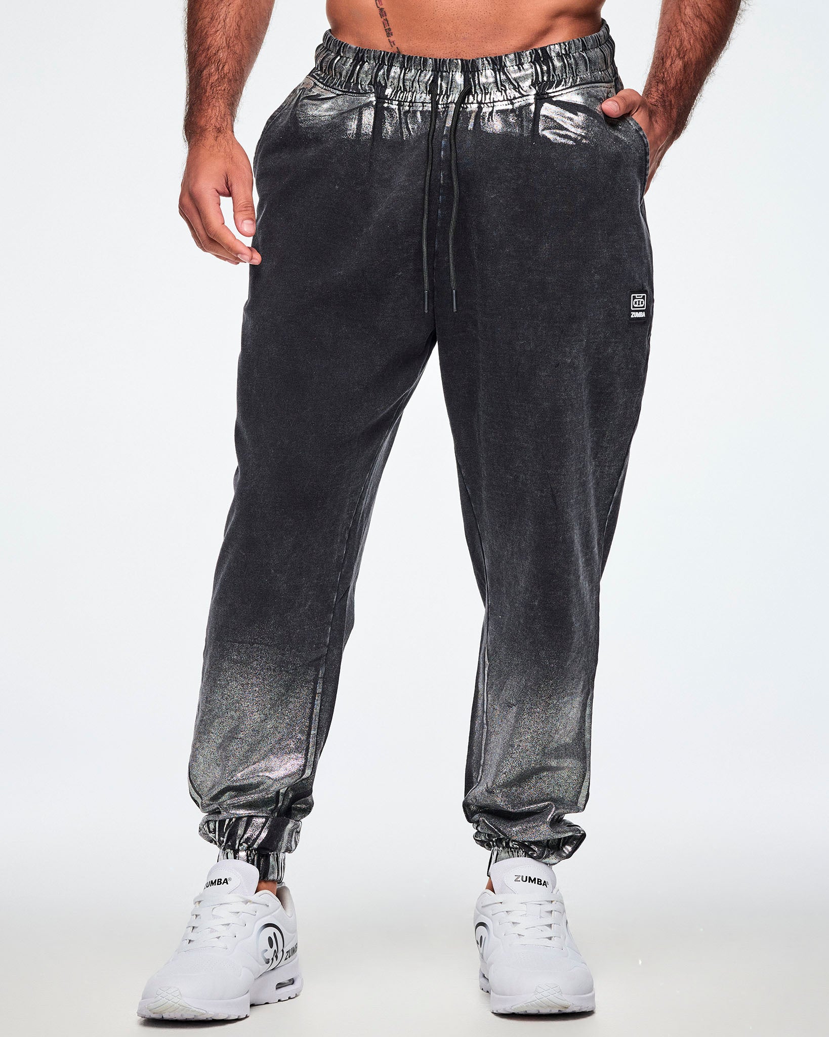 Front view of a male model wearing black and silver dark acid-wash sweatpants with a subtle tonal pattern, featuring a drawstring elastic waist, side pockets, and elastic cuffs, paired with white shoes.