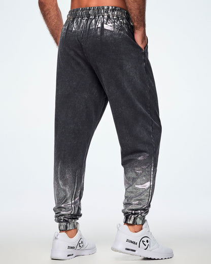 Back view of a male model wearing black and silver dark acid-wash jogger sweatpants with a subtle tonal pattern, featuring side pockets and elastic cuffs, paired with white shoes.