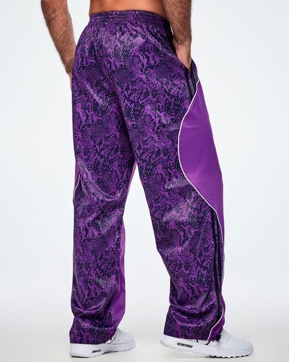A male model from the back, wearing purple track pants with a snakeskin-style patterned back, paired with white shoes. 