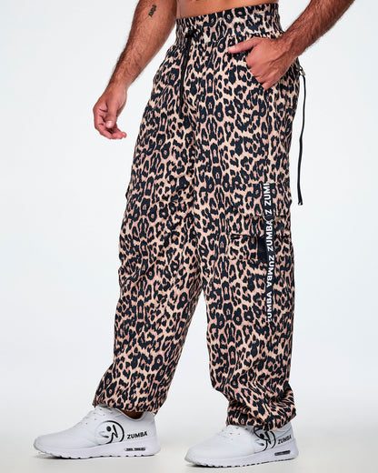 A male model wearing tan leopard print cargo pants with black Zumba straps on the pockets, paired with white shoes.