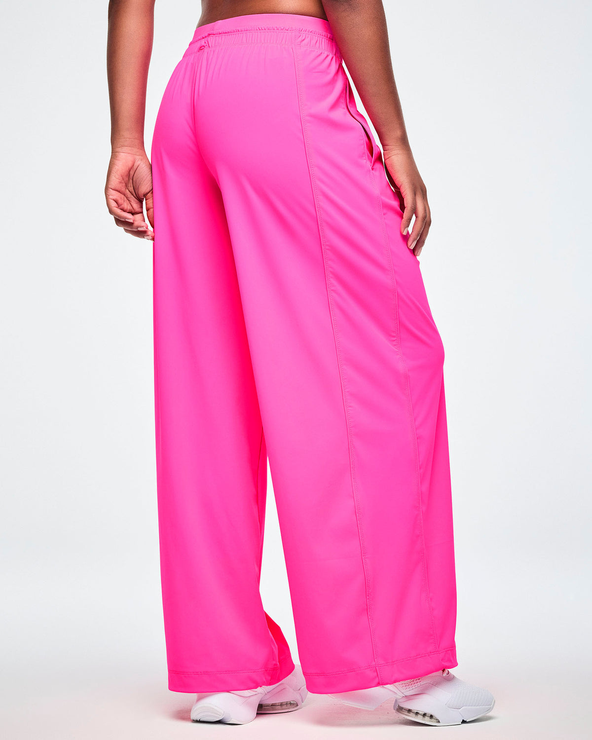 A female model shown from the back wearing pink slouch pants and white shoes, against a white background.